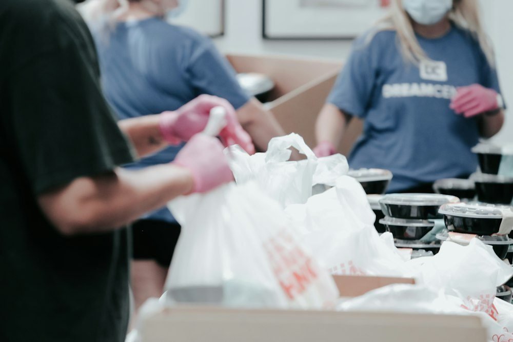 Volunteers wearing gloves pack food into white bags