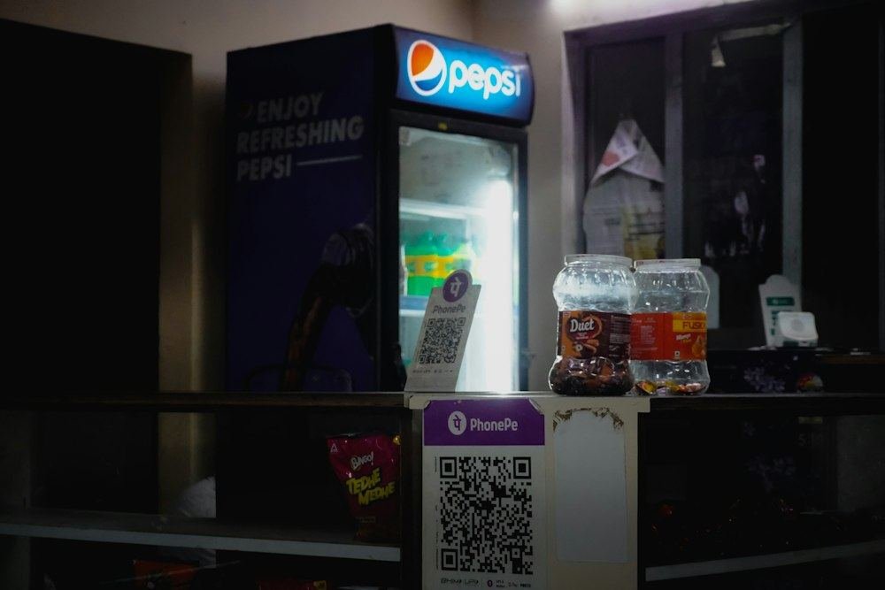 A merchant QR-code payment display stands beside a drinks cooler and shop goods