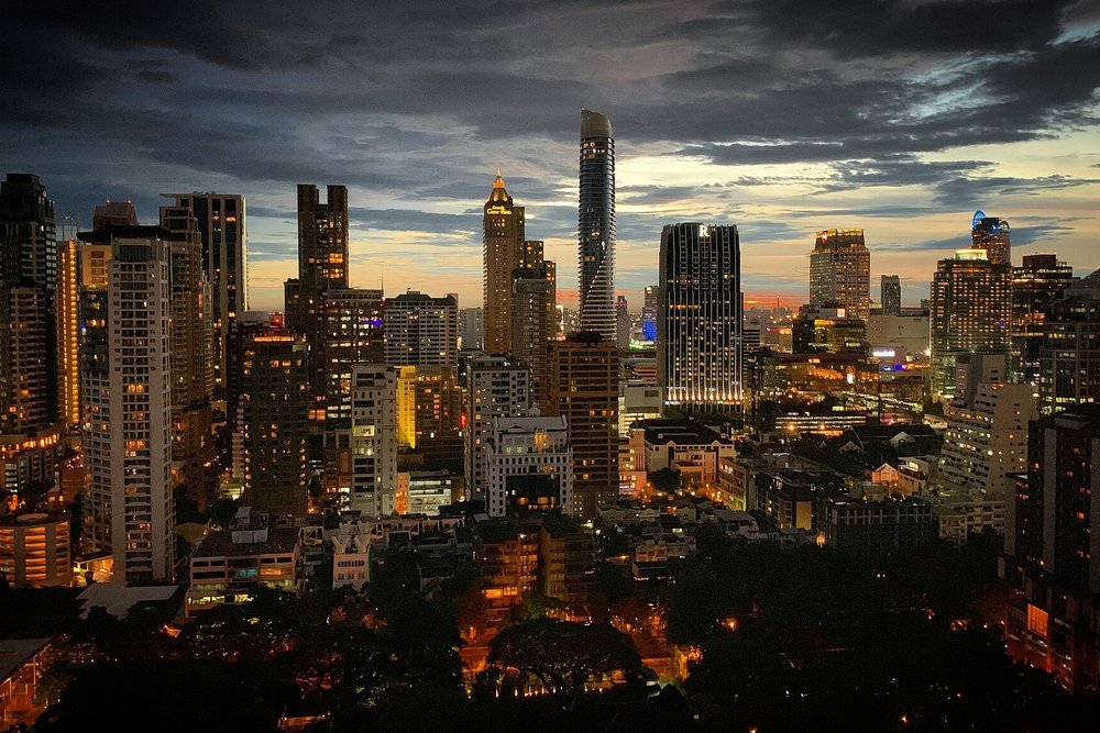Twilight envelops the modern skyline of Bangkok's Ratchadamri district. Skyscrapers dominate the scene, illuminated by city lights against a…